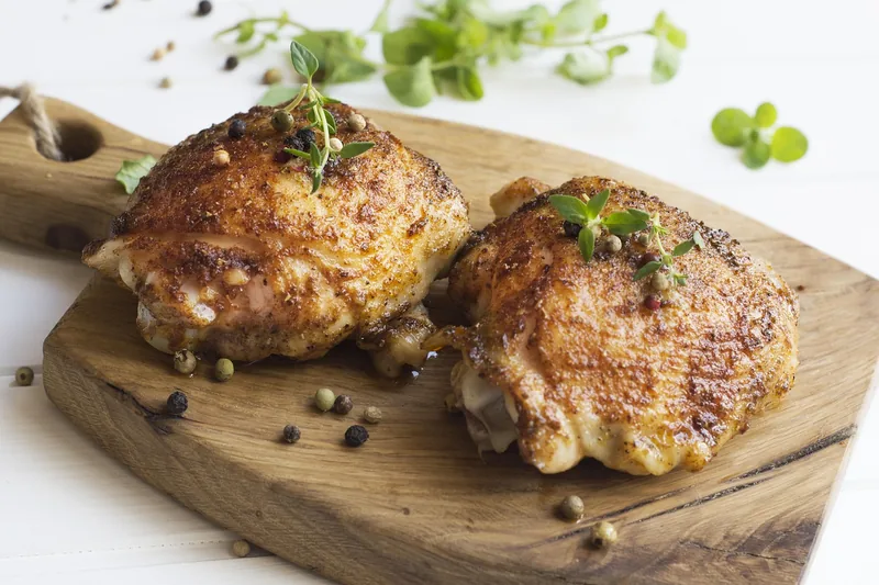 Two crisp-skinned chicken thighs on a wooden board with herbs