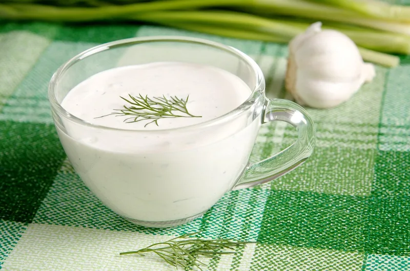 A jug of garlic cream sauce with dill and a garlic bulb