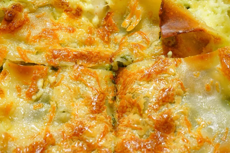 Close-up of a cheesy casserole, browned in patches and bubbling