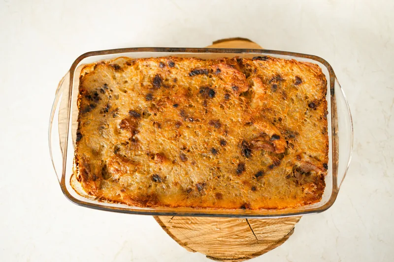 A deep casserole in a glass dish with a browned, crusted top, cooling on a wooden rack