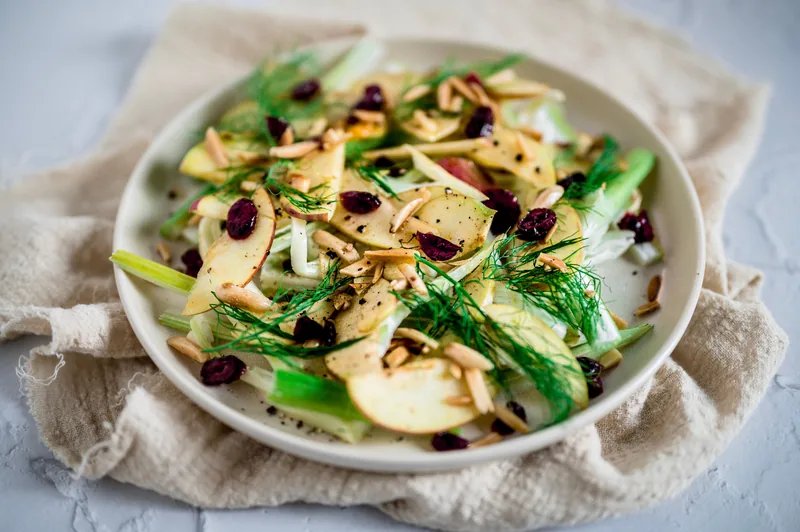 Sliced apple, dried cranberries and toasted nuts over greens in a shallow bowl