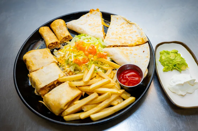 A plate of browned rolled tortilla parcels cut open, served with fries, salsa and guacamole
