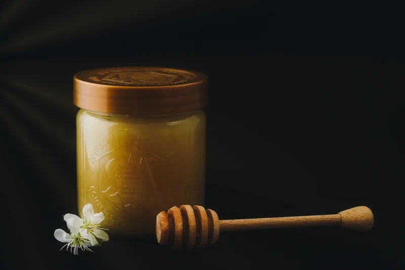 A jar of honey with a wooden dipper resting beside it