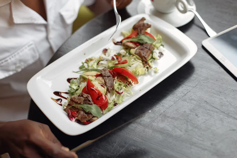 A long white plate of dressed salad leaves topped with strips of grilled beef, held at the table