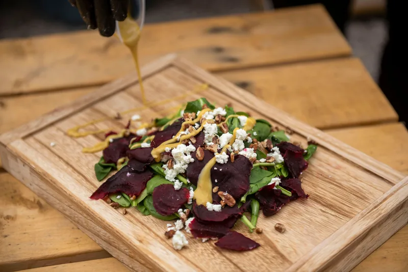 Oil being poured over beet and cheese on a board