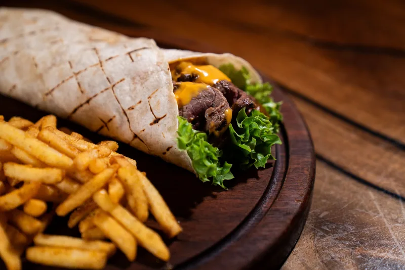 A griddled wrap cut open to show beef and lettuce, fries alongside