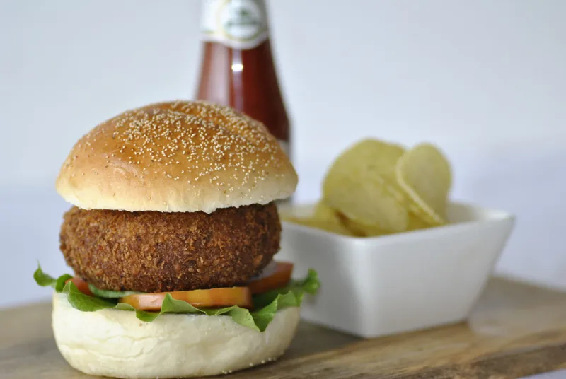 A veggie burger with a thick browned patty, lettuce and tomato in a sesame bun, fries alongside