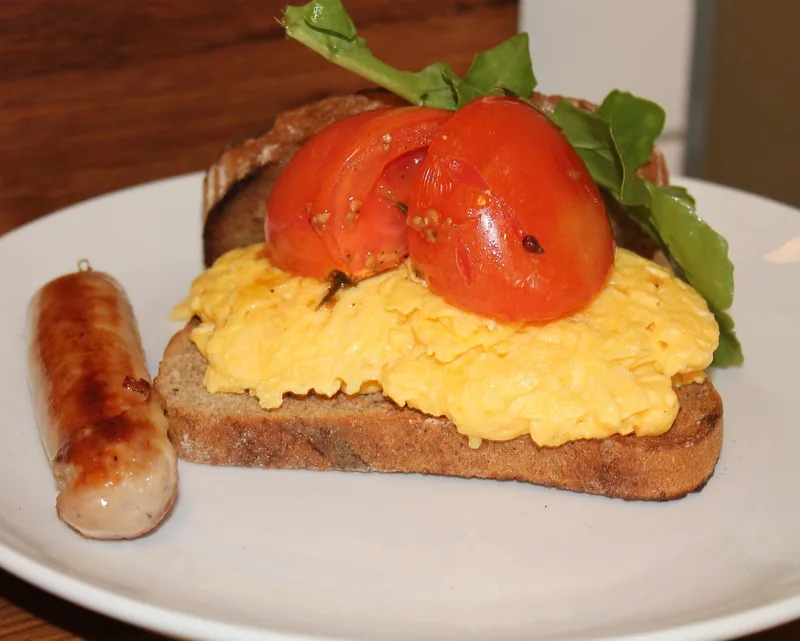 Scrambled eggs on toast with a sausage and a grilled tomato