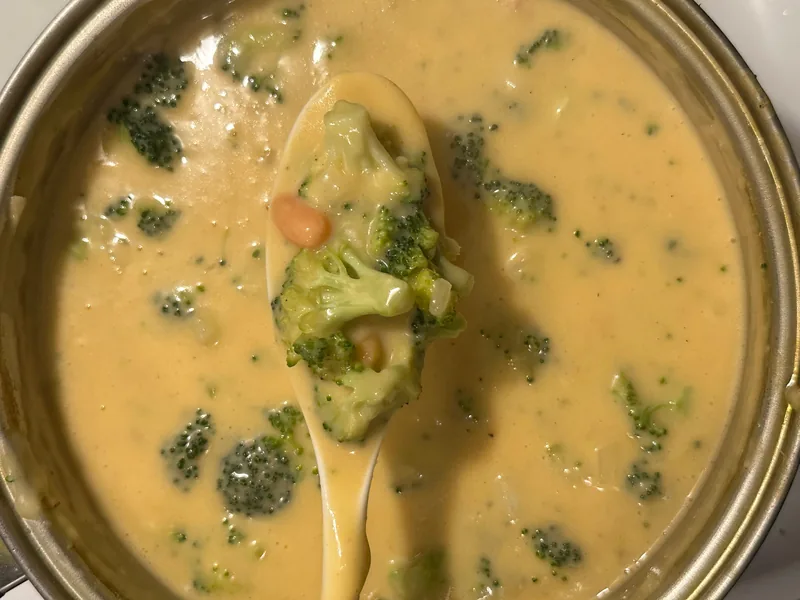 A pot of broccoli cheddar soup with a spoon lifting a floret