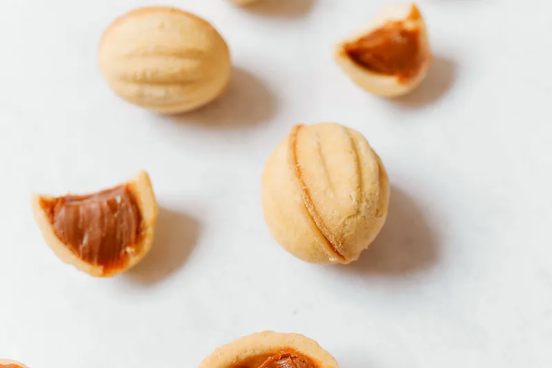 Pale dome-shaped cookies, one broken open to show a caramel filling
