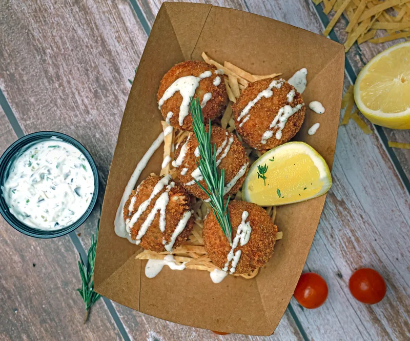 Browned round cakes on kraft paper with a lemon wedge, a herb dip and a pale drizzle over the top