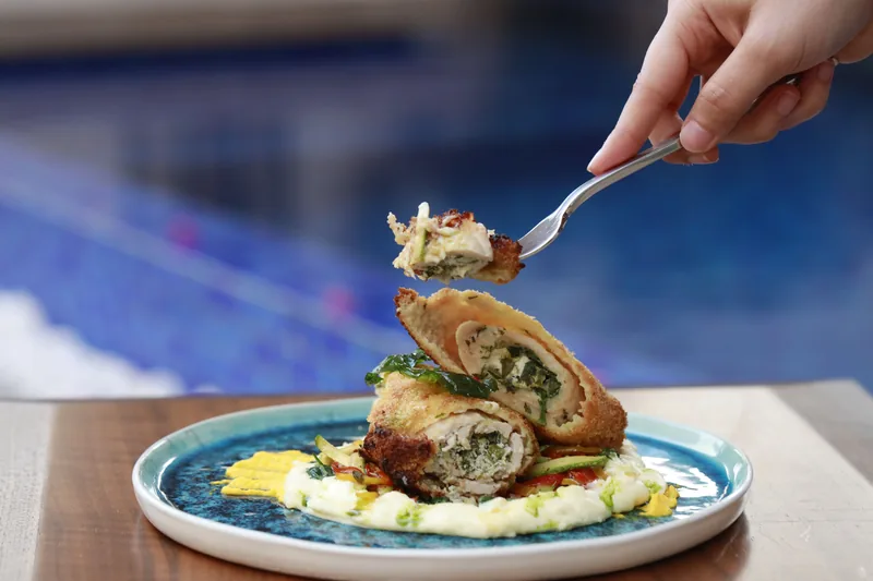 A fork lifting a slice of stuffed chicken roll, the dark herb and mushroom filling visible in cross-section