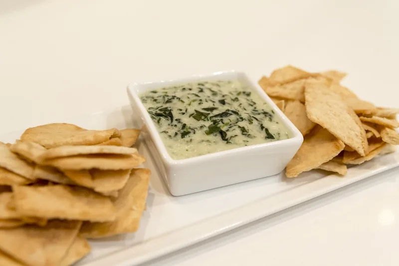 A white dish of spinach dip surrounded by pita chips