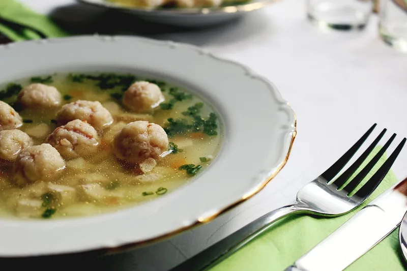 A bowl of broth with small dumplings and parsley