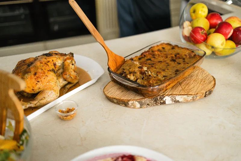 A baked rice casserole in a glass dish with a serving spoon and a roast chicken beside it