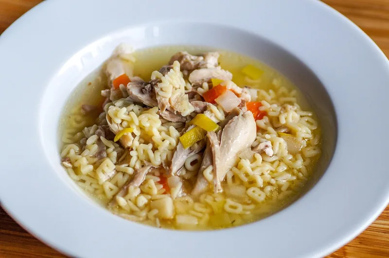 A shallow bowl of clear broth with shredded chicken and small pale pasta shapes