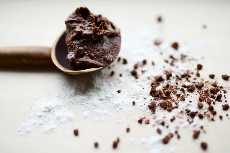 A spoonful of chocolate frosting beside scattered cocoa