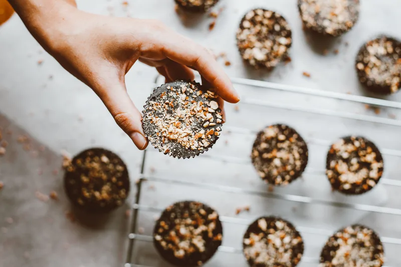 A hand placing nut-studded chocolate clusters in rows on a baking sheet