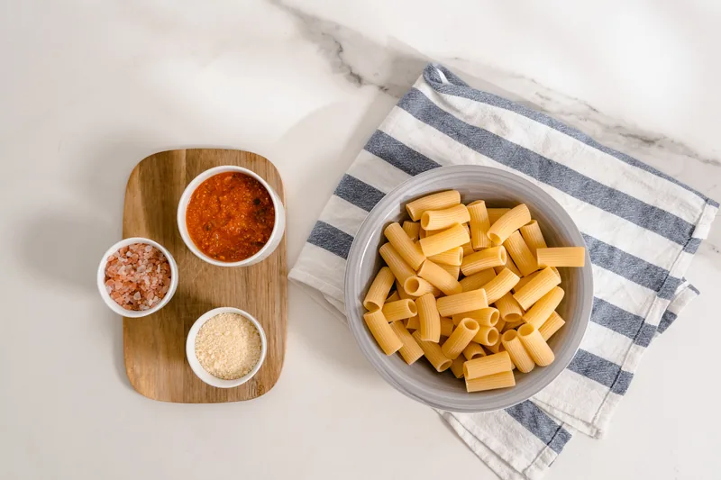 A bowl of dried rigatoni beside small bowls of spices