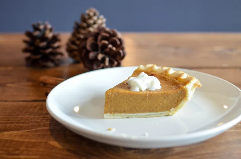 A slice of pumpkin pie with whipped cream on a white plate