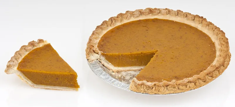 A whole pumpkin pie with one slice cut and set beside it