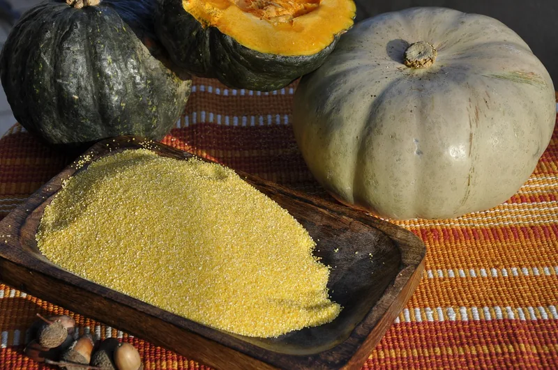 A board of coarse yellow cornmeal beside winter squash