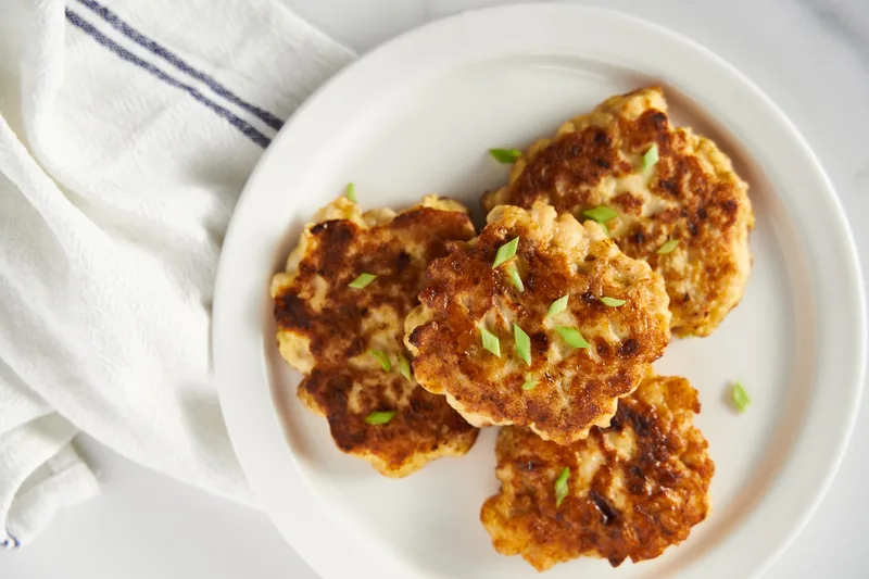 Three golden fried patties flecked with green onion on a white plate