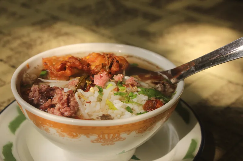 A bowl of thick soup with rice, meat and vegetables