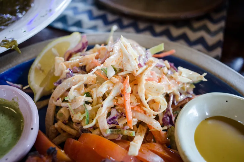 A bowl of creamy coleslaw with finely shredded cabbage and carrot, lemon and a dish of dressing beside it