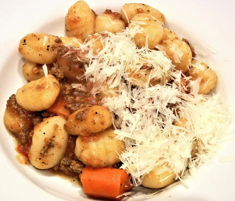 Gnocchi with carrot and a heap of grated parmesan on a white plate