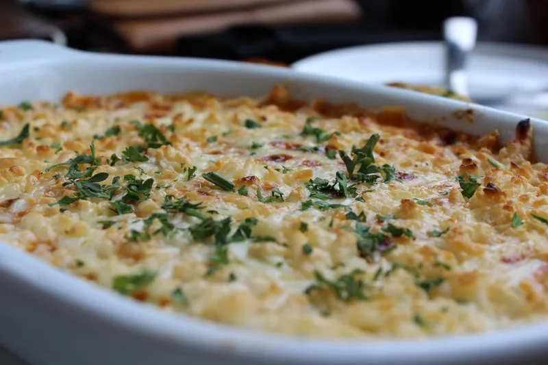 A creamy baked casserole in a white dish, browned on top and scattered with herbs