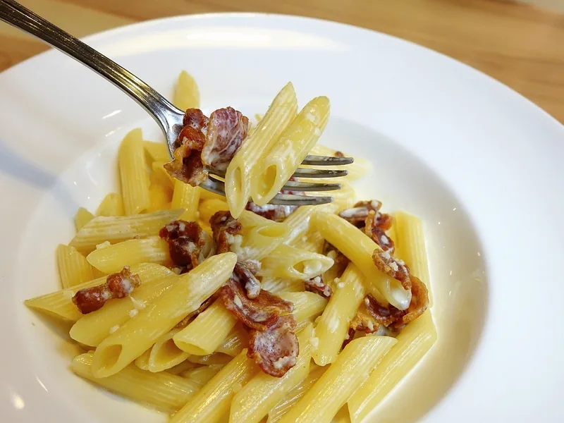 Penne with pieces of browned sausage on a white plate, a fork resting in it