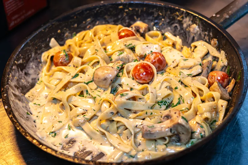 A skillet of creamy pasta with sliced sausage, mushrooms and cherry tomatoes