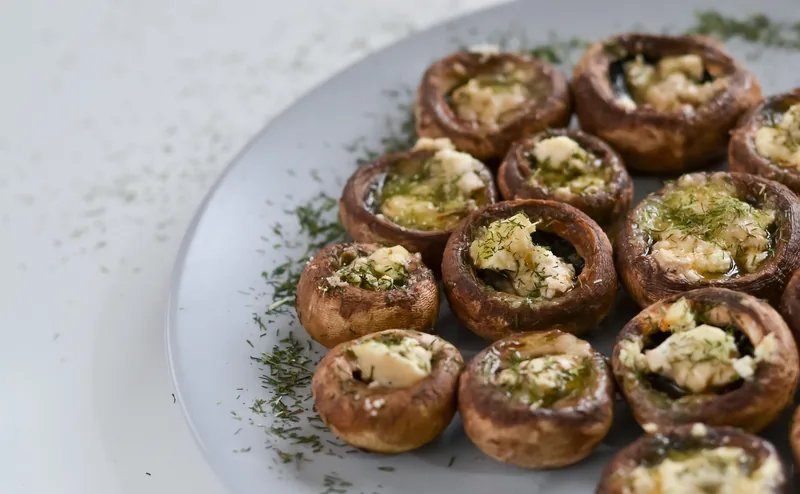 A plate of baked stuffed mushroom caps scattered with chopped herbs