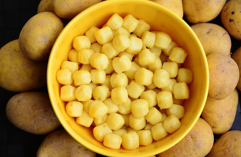 A bowl of uncooked gnocchi surrounded by potatoes