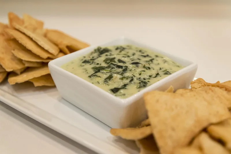 Spinach artichoke dip in a square dish with pita chips