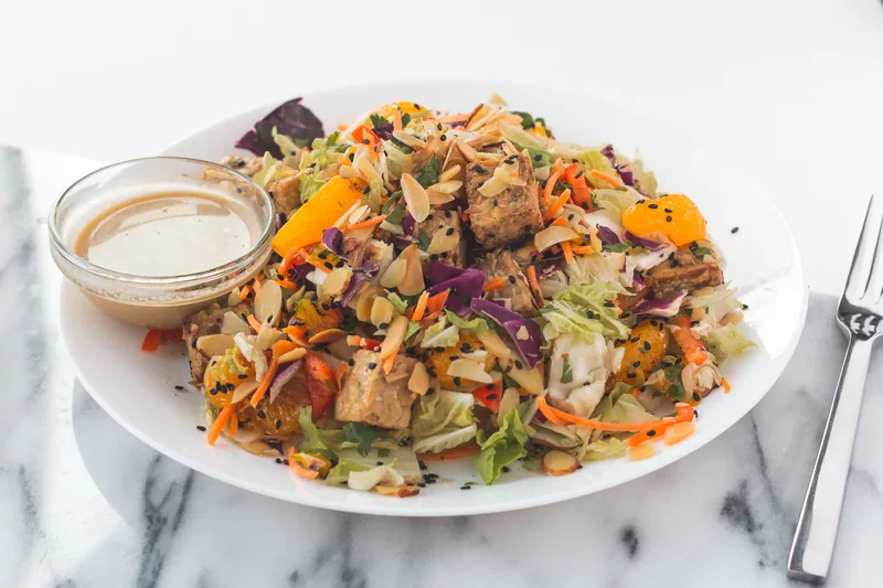 A crunchy mixed salad with carrot and cabbage, dressing alongside