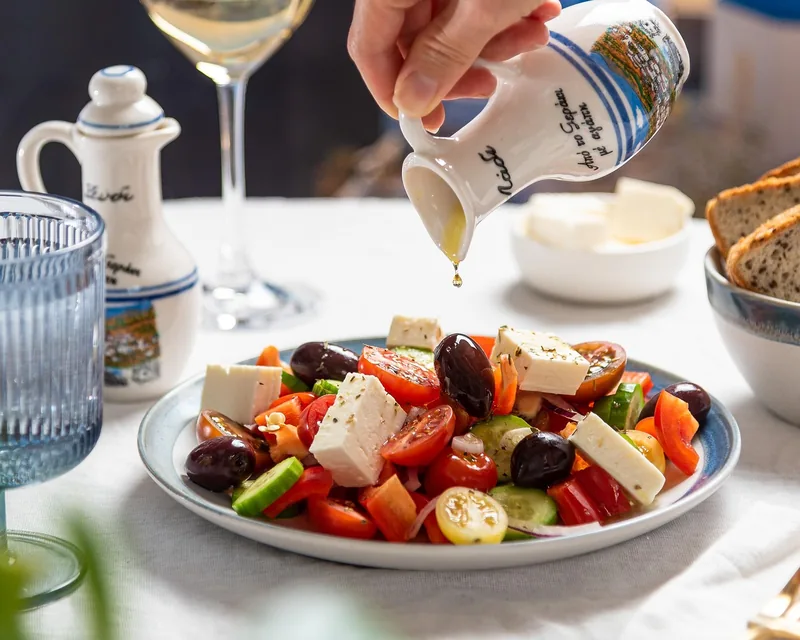 Dressing being poured over a salad with feta and olives