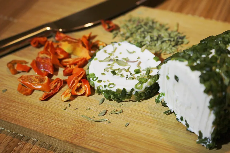 A soft cheese log rolled in chopped herbs on a wooden board