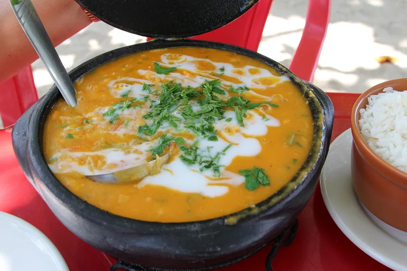 A dark pot of creamy orange fish stew finished with cilantro, rice alongside