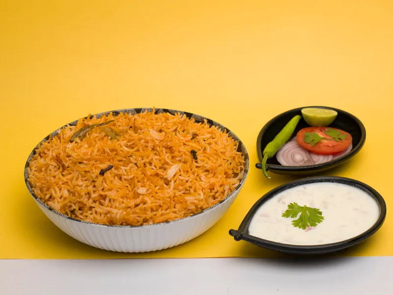 A bowl of tomato-red rice with small bowls of salsa and cream beside it
