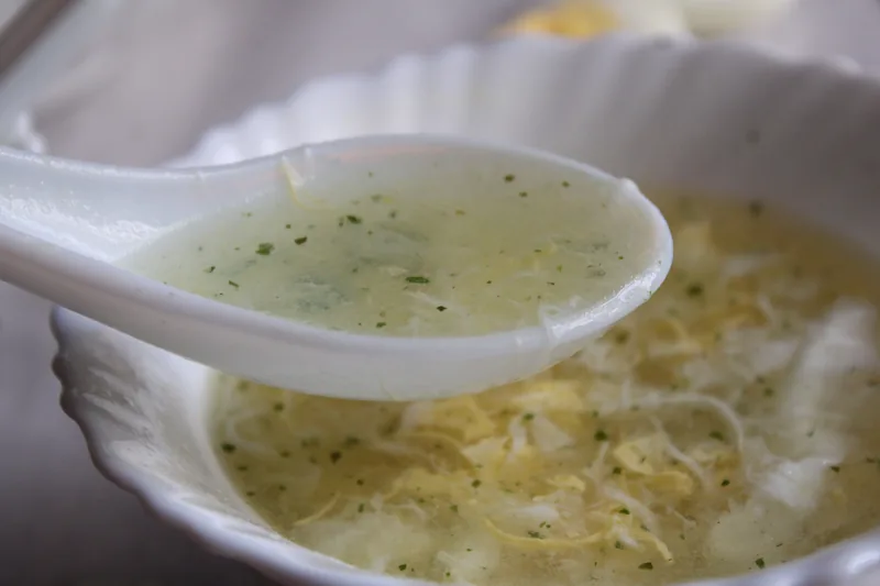 A bowl of egg drop soup with a white porcelain spoon
