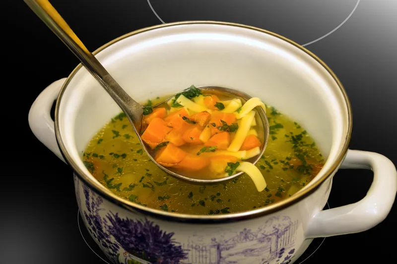 A spoon lifting broth, carrot and noodles from the bowl