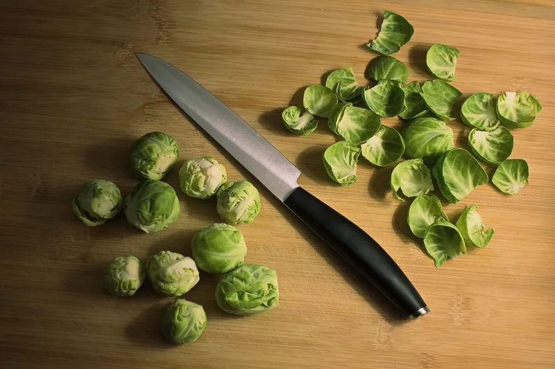 Brussels sprouts and loose leaves on a wooden board beside a knife