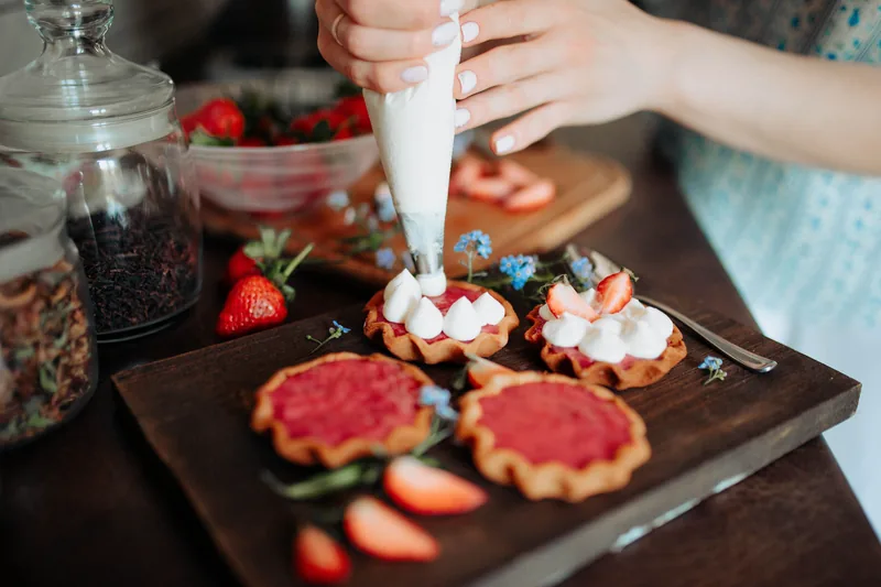 Cream being piped onto cookie bases beside strawberries and blueberries