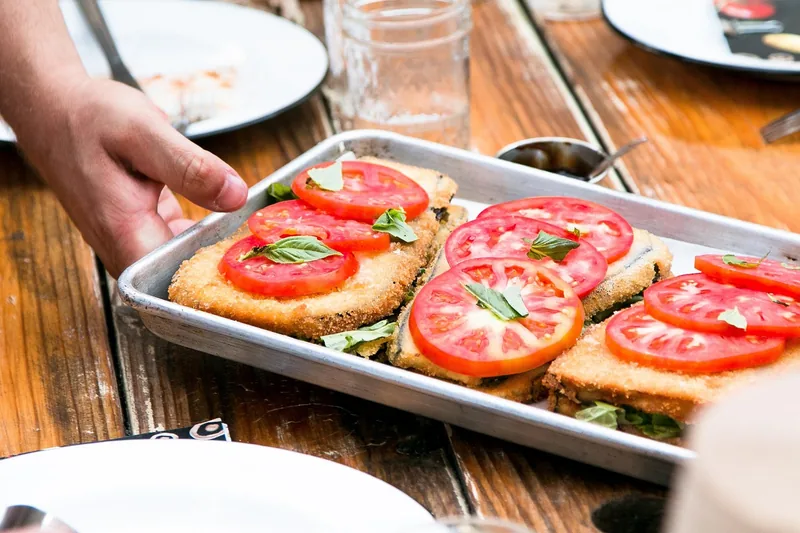 Breaded fried slices topped with fresh tomato on a sheet pan