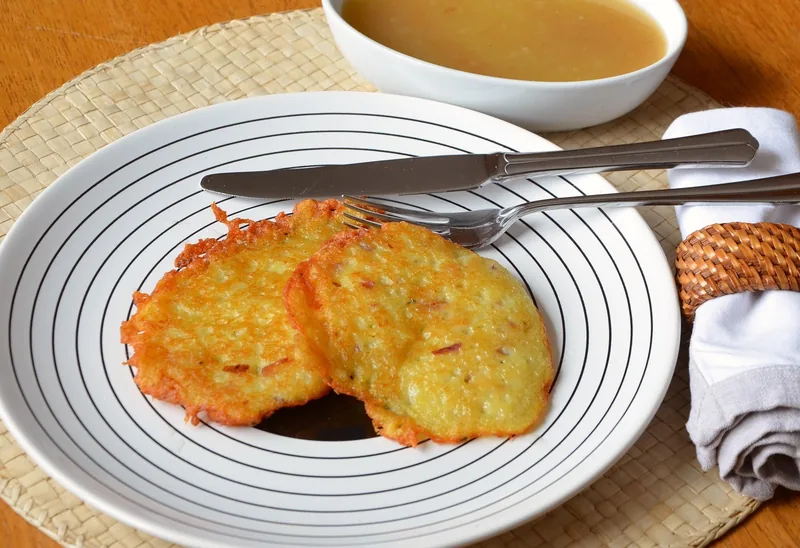 Two potato pancakes on a plate with a bowl of apple sauce