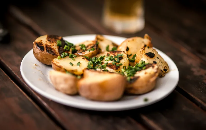 Herbed potatoes on a plate with a glass behind