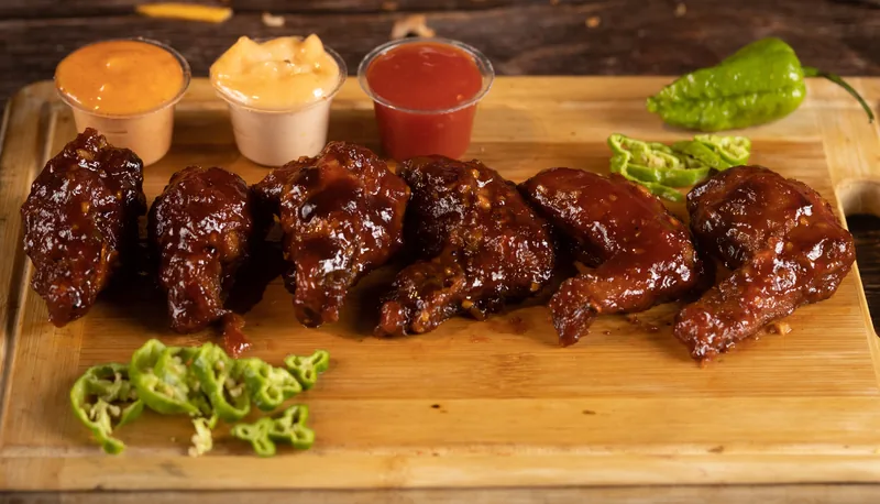 Barbecue-glazed chicken on a board with cups of sauce