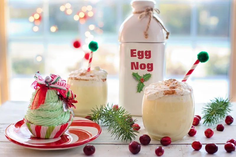 Eggnog poured into glasses beside a bottle, dressed for Christmas